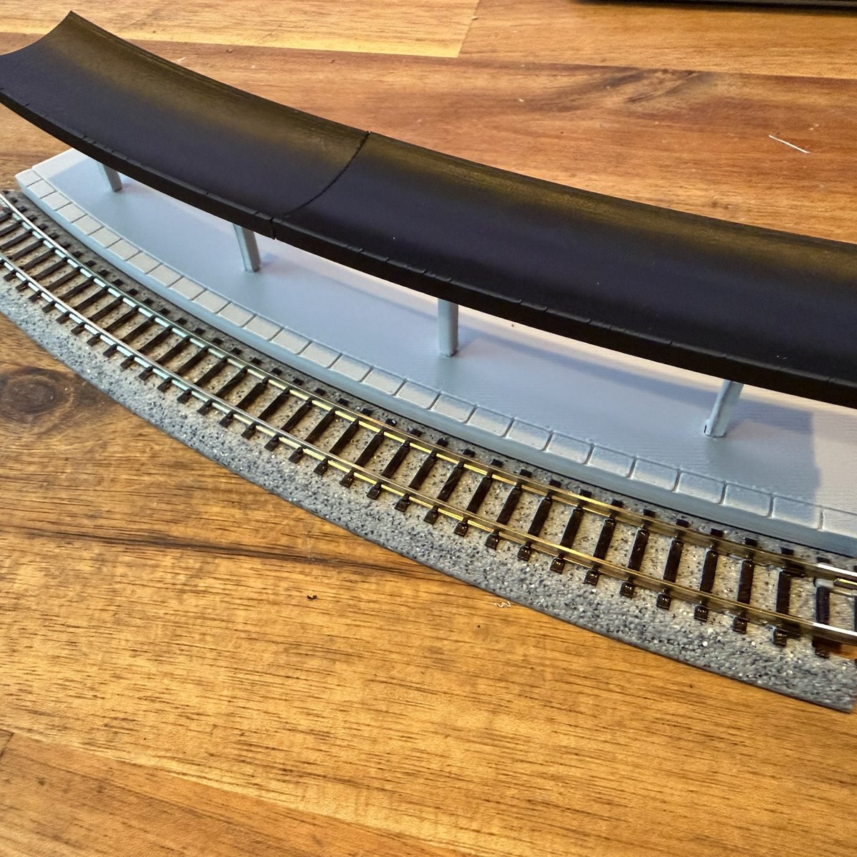 Real print: the N scale curved station with black canopy on its light grey platform beside a Kato Unitrack R381 curve