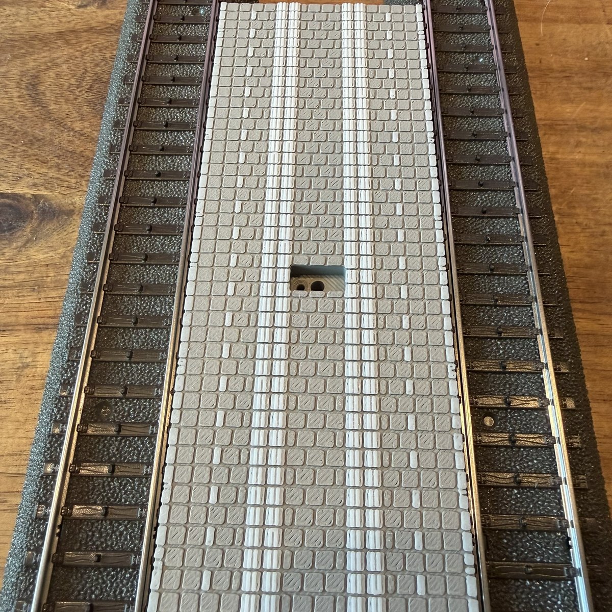 Real print: the platform deck from above, tile field with the white tactile guidance strip and safety bands, pillar socket in the middle
